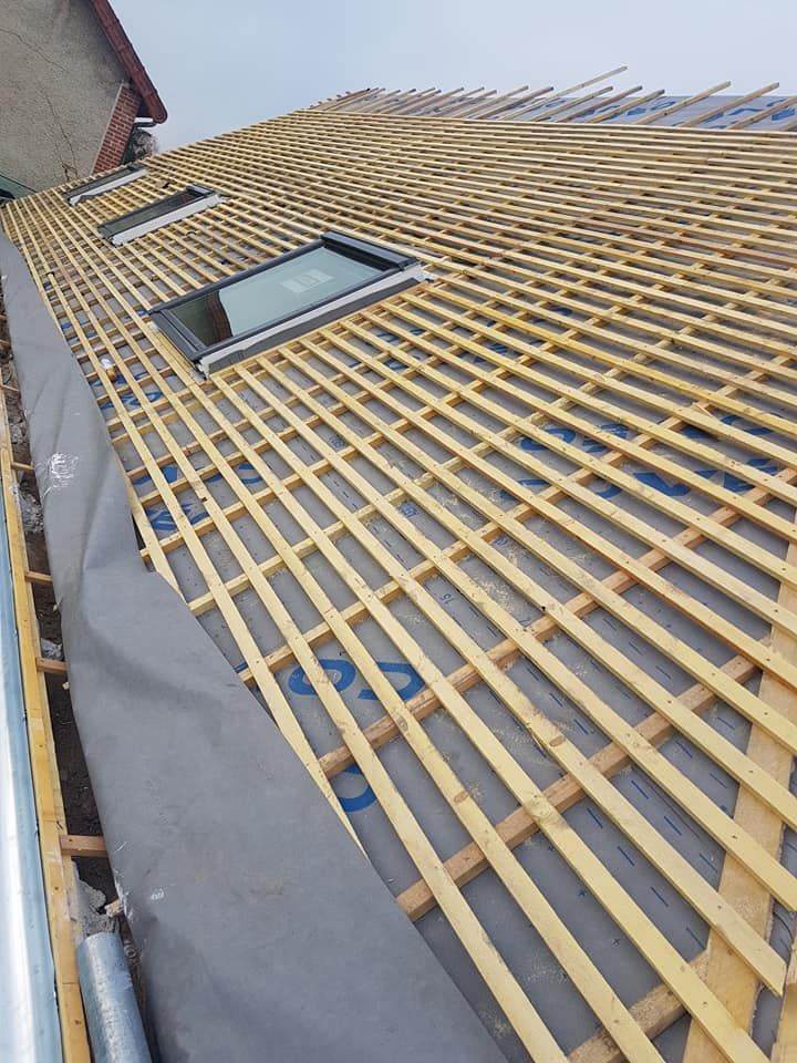 Toiture à liteaux en bois, avec une fenêtre de toit et une sous-couche grise sur un toit en pente.