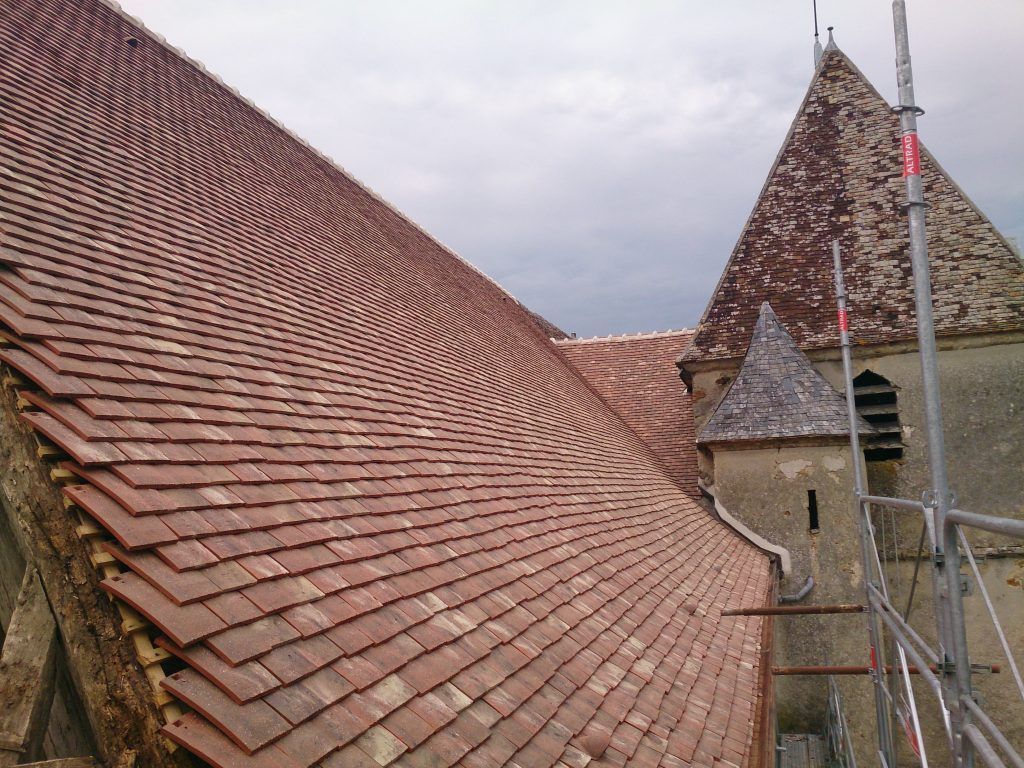 Toits d'église en tuiles rouges et tour en pierre sous un ciel nuageux, vus d'en haut
