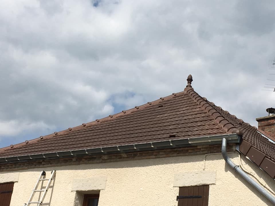 Toit de maison en tuiles brunes et mur extérieur blanc sous un ciel nuageux