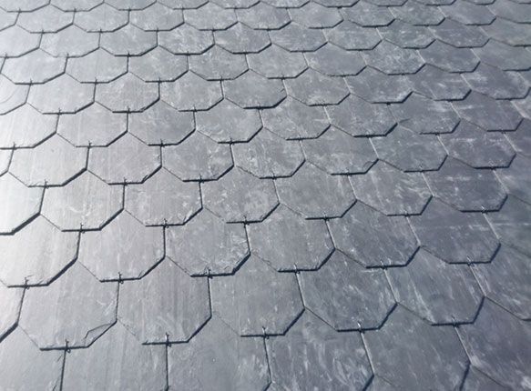 Gros plan sur des bardeaux hexagonaux gris à la surface texturée et patinée.