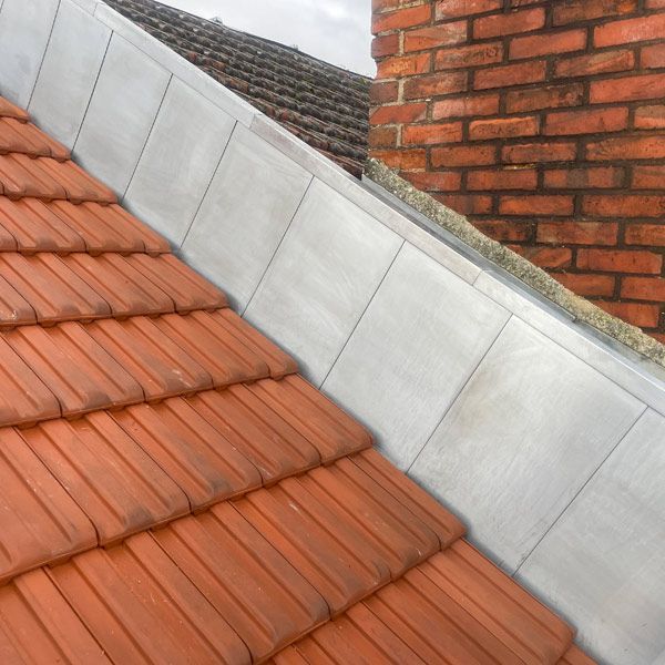 Jonction d'un toit de tuiles rouges et grises à côté d'une cheminée en briques sur une maison
