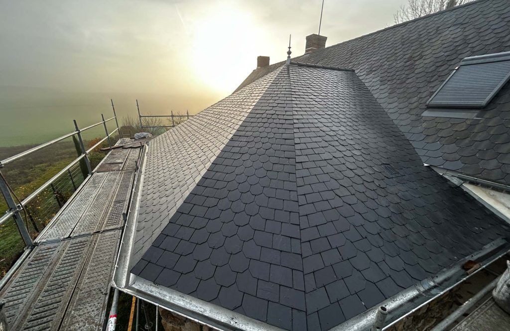 Maison au toit d'ardoise en cours de réparation au coucher du soleil, avec des échafaudages le long du côté gauche.