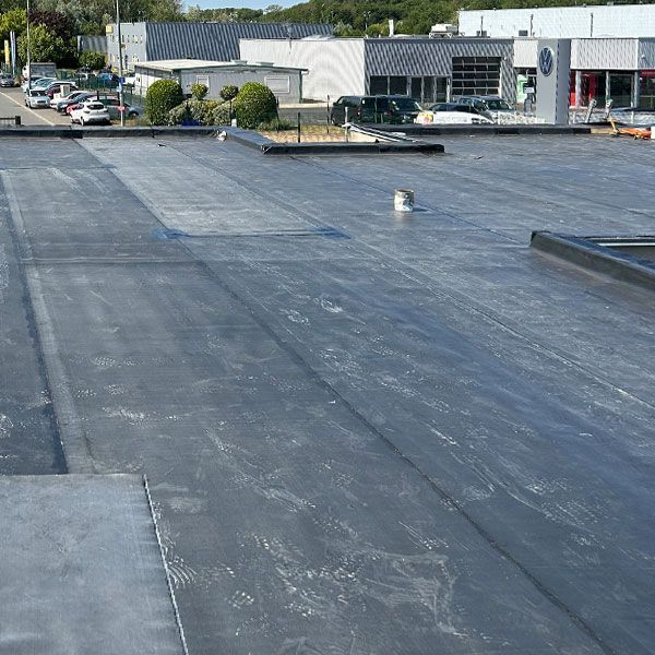 Toit plat commercial avec toiture grise, aérations et bâtiments de parking en arrière-plan.