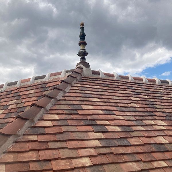 Toit de tuiles avec une flèche décorative sous un ciel nuageux