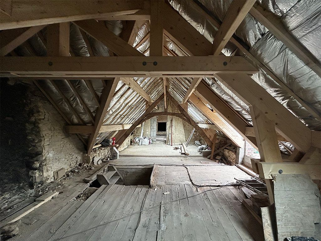 Grenier en rénovation avec poutres apparentes, isolation et plancher brut.