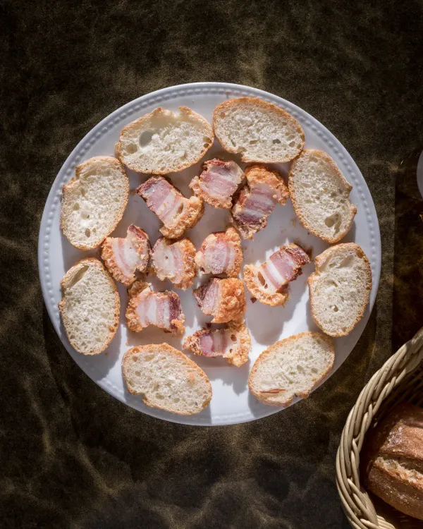 Un plato blanco cubierto con pan y tocino junto a una canasta de pan.