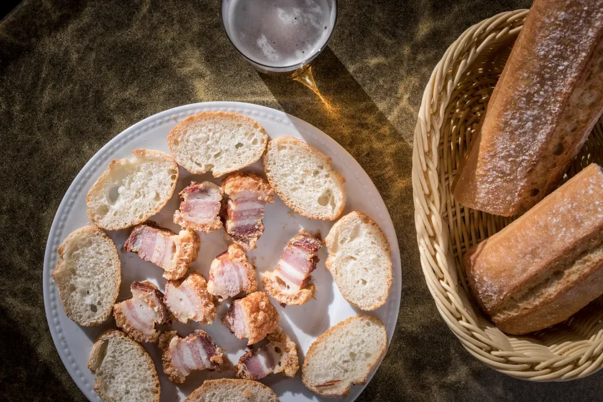 Un plato de comida junto a una cesta de pan y un vaso de cerveza sobre una mesa.
