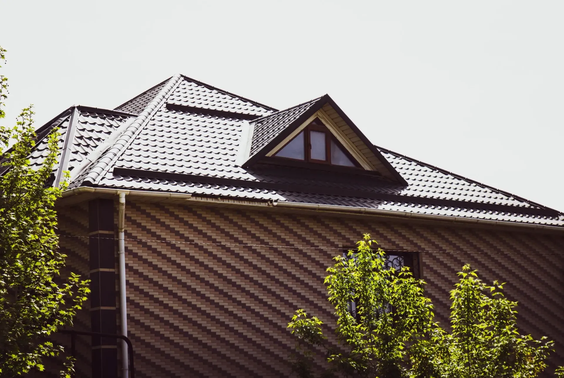 Casa con exterior con diseño de ladrillo y techo oscuro y texturizado; se ve una buhardilla con ventanas.