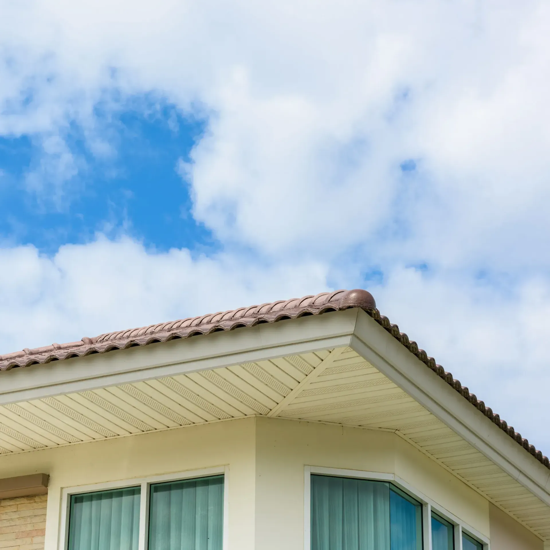 Línea del tejado de una casa blanca con techo de tejas contra un cielo azul parcialmente nublado.
