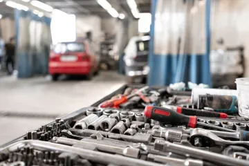 Primer plano de herramientas de mecánico en una bandeja con un coche rojo al fondo, en un garaje.