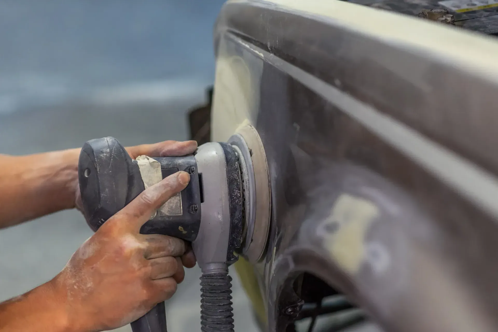 Manos lijando la carrocería del coche con lijadora eléctrica.