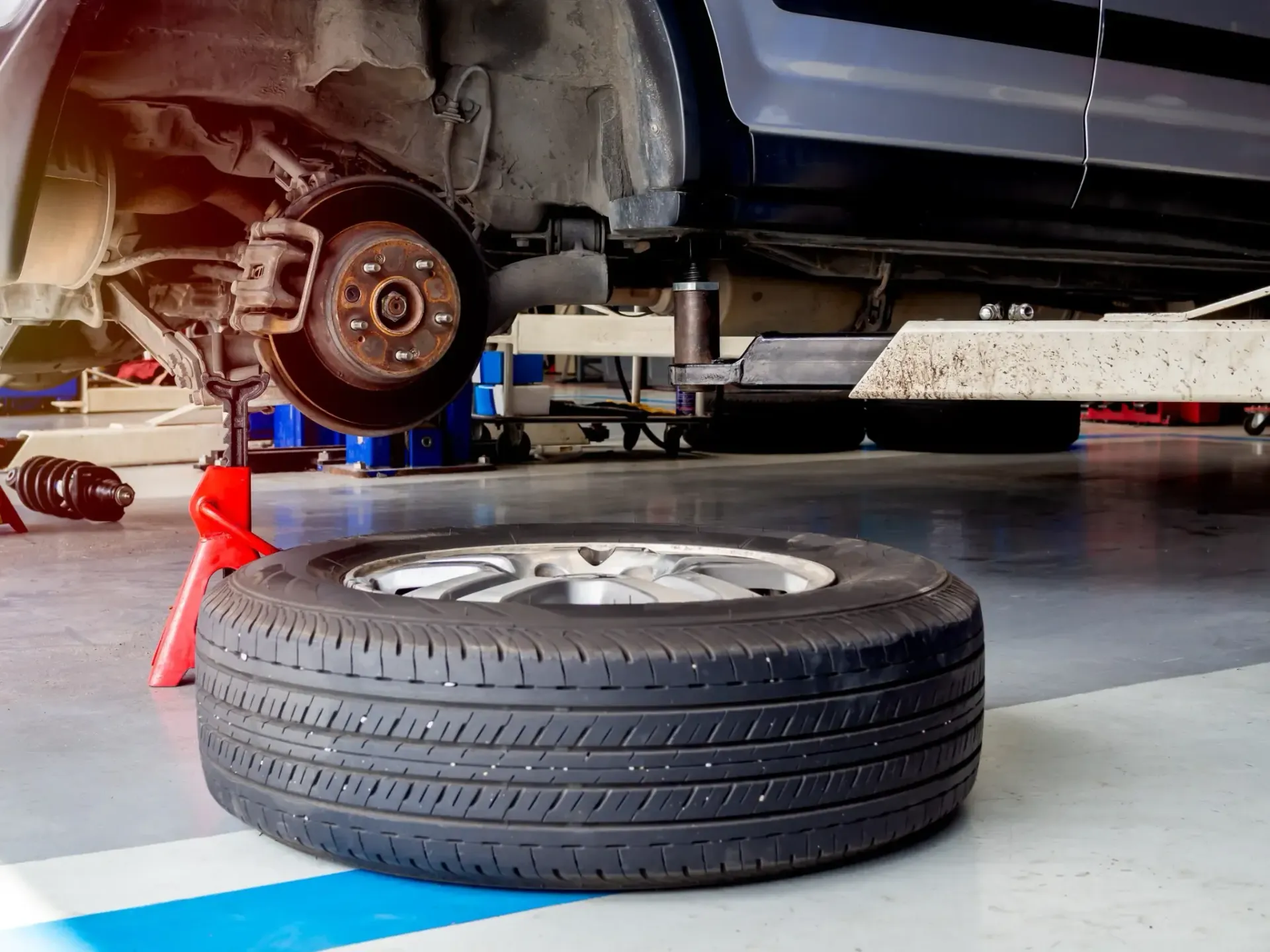 Se está trabajando en un automóvil en un garaje, con una rueda quitada y sostenida por un gato