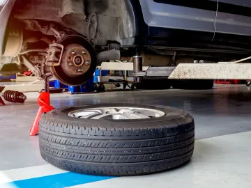 Se está trabajando en un automóvil en un garaje, con una rueda quitada y sostenida por un gato