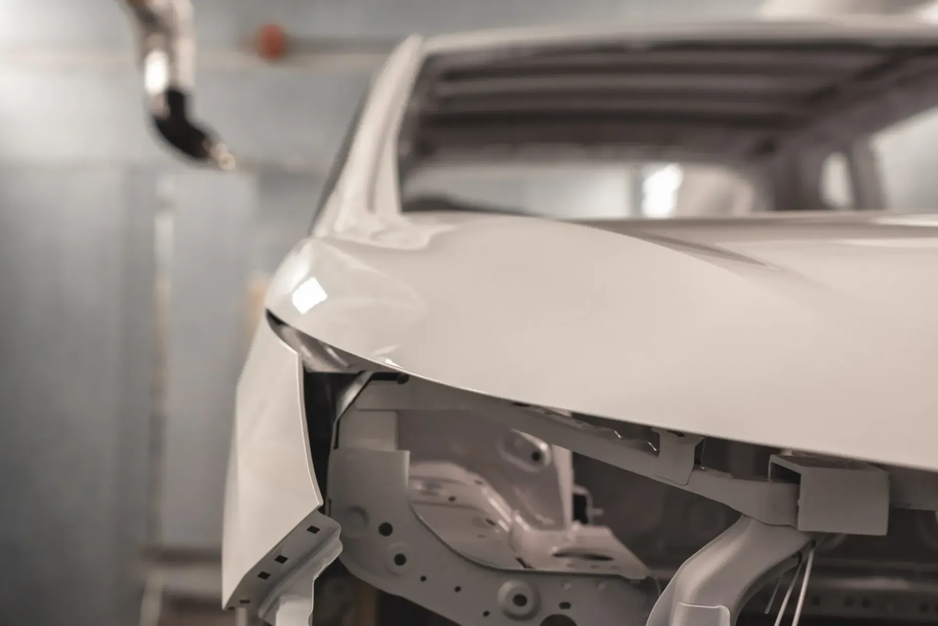 Chasis de coche blanco en una cabina de pintura que recibe la pintura mediante un brazo robótico.