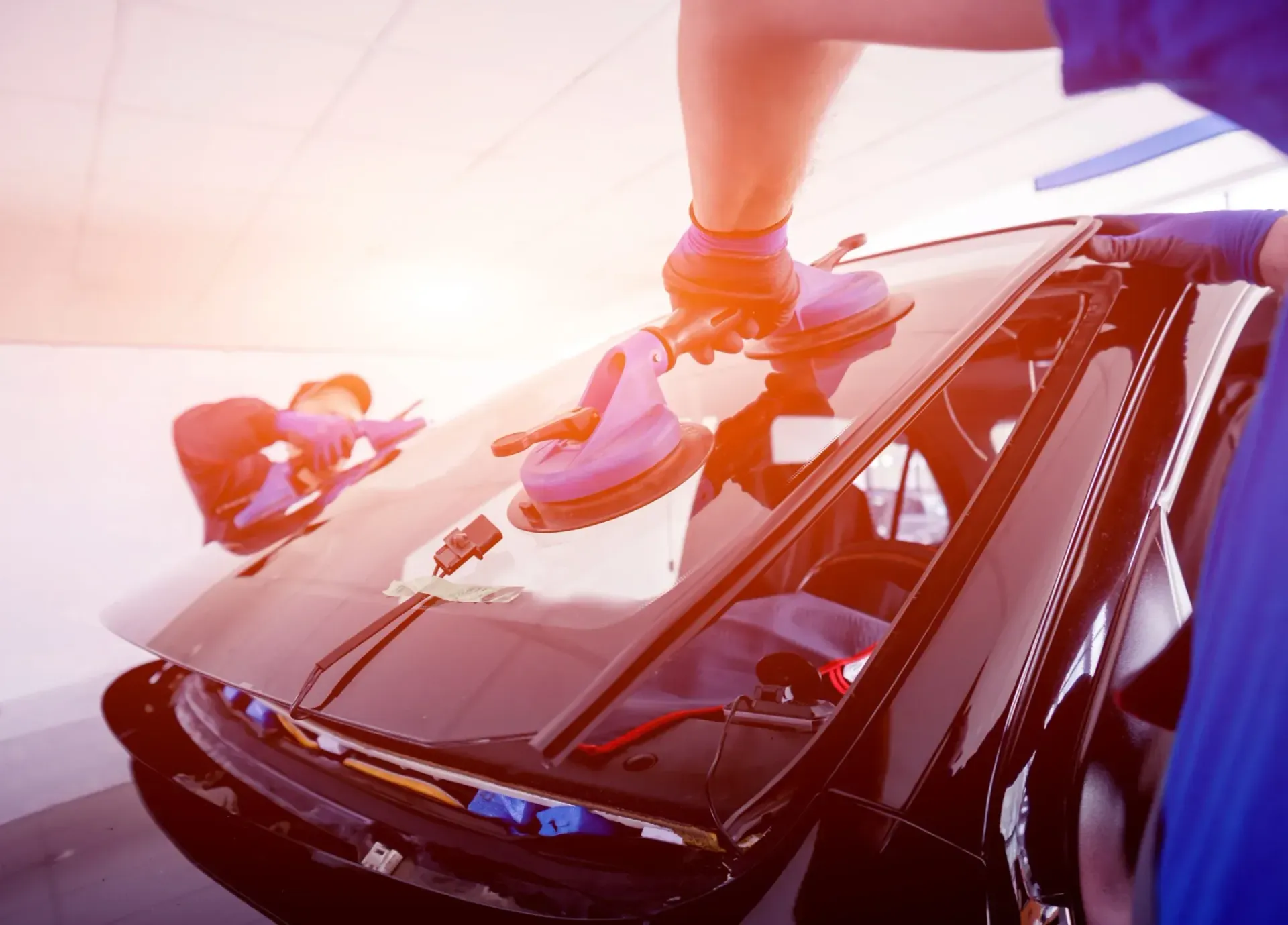 Una persona instalando un parabrisas de coche negro, utilizando ventosas para sujetar el cristal.