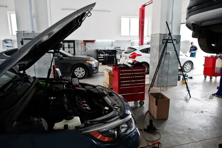 Taller de reparación de automóviles; vehículos en reparación con capós abiertos, herramientas y un trabajador al fondo.