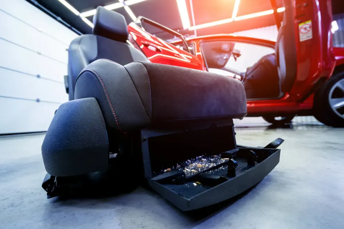 Asiento de automóvil retirado de un automóvil rojo, mostrando un compartimiento de almacenamiento abierto con escombros.