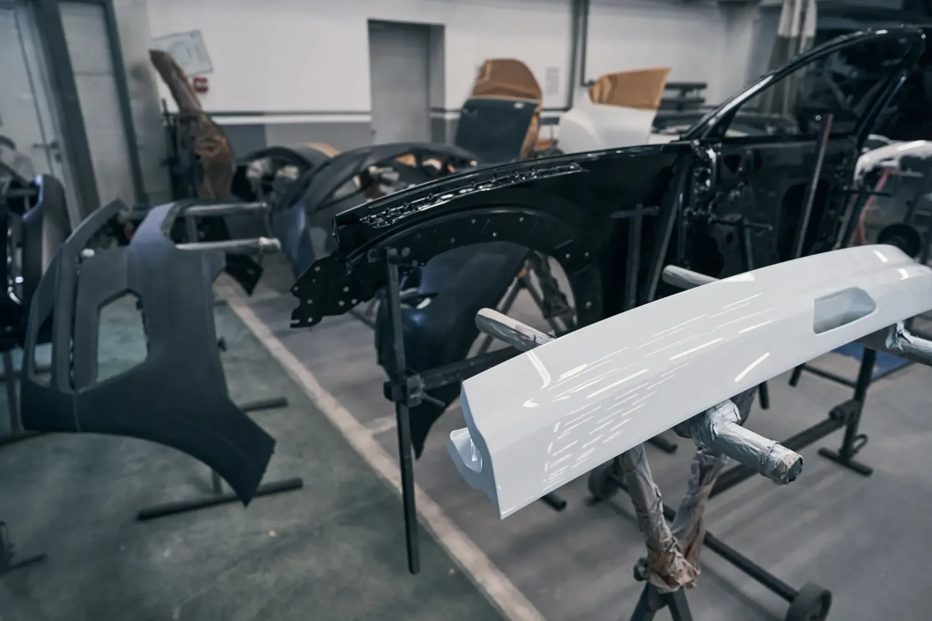 Piezas de coche en diversas etapas de montaje en un taller. Se aprecia un chasis negro parcialmente ensamblado.