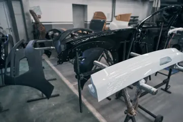 Piezas de coche en diversas etapas de montaje en un taller. Se aprecia un chasis negro parcialmente ensamblado.
