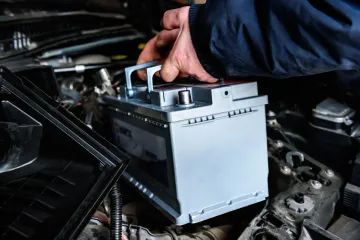 Persona instalando una batería de automóvil en el compartimiento del motor de un vehículo.
