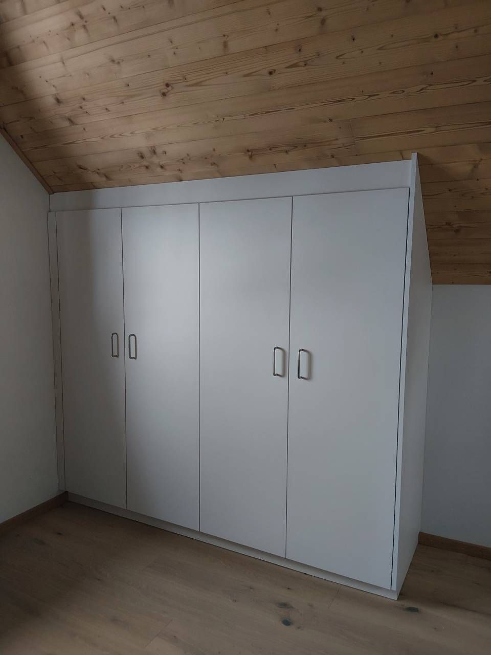 Weisser Einbauschrank mit vier Türen in einem Zimmer mit holzgetäfelter Decke und hellem Holzboden