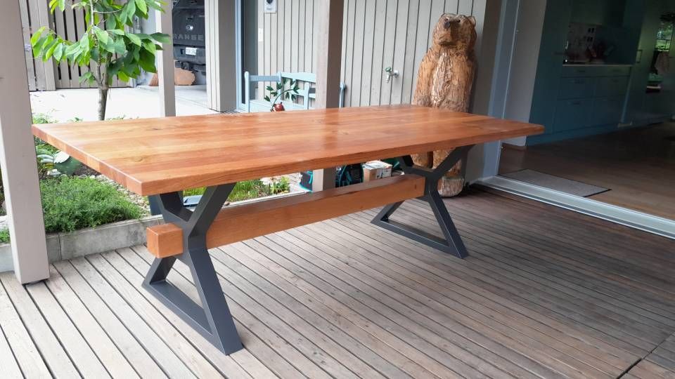 Ein Holztisch auf einer Terrasse vor einem modernen Haus, im Hintergrund ein Stuhl.