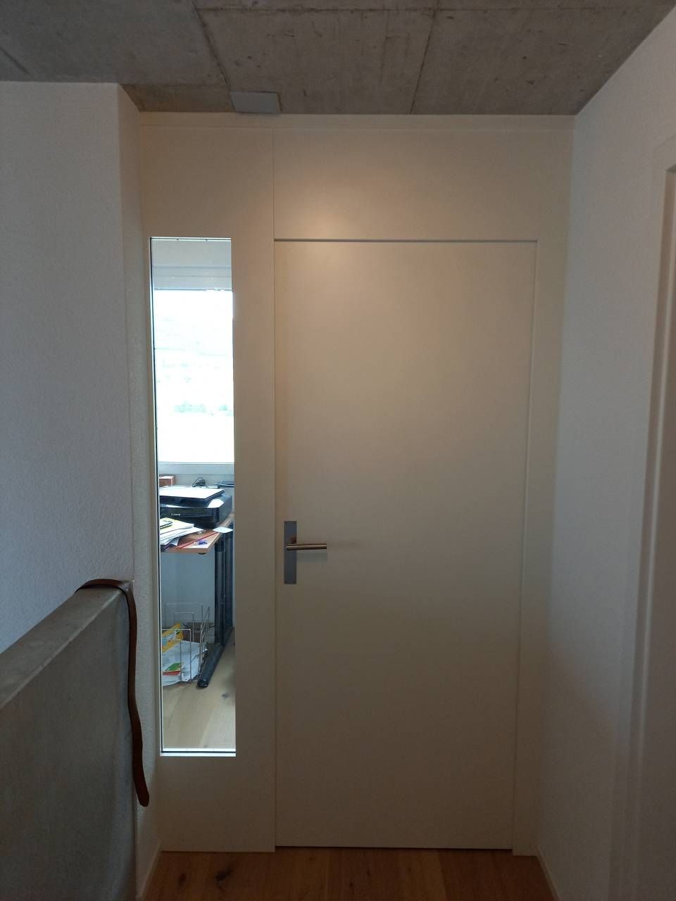 Innenflur mit einer geschlossenen weissen Tür und einem schmalen Fenster daneben.