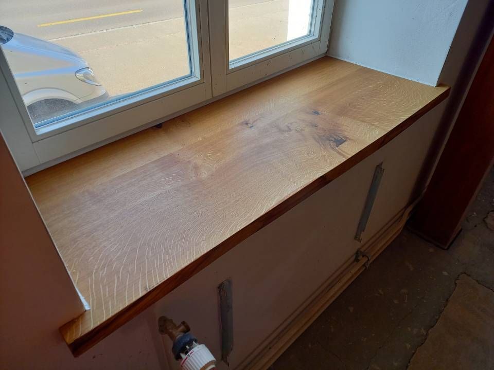 Fensterbank und Schrank aus Holz mit einem darunter angebrachten Wasserhahn in einem Zimmer.
