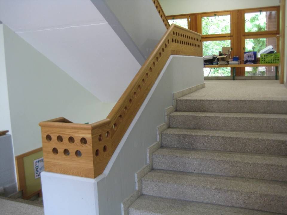 Innentreppenhaus mit Teppichstufen und einem hölzernen Handlauf neben grossen Fenstern.
