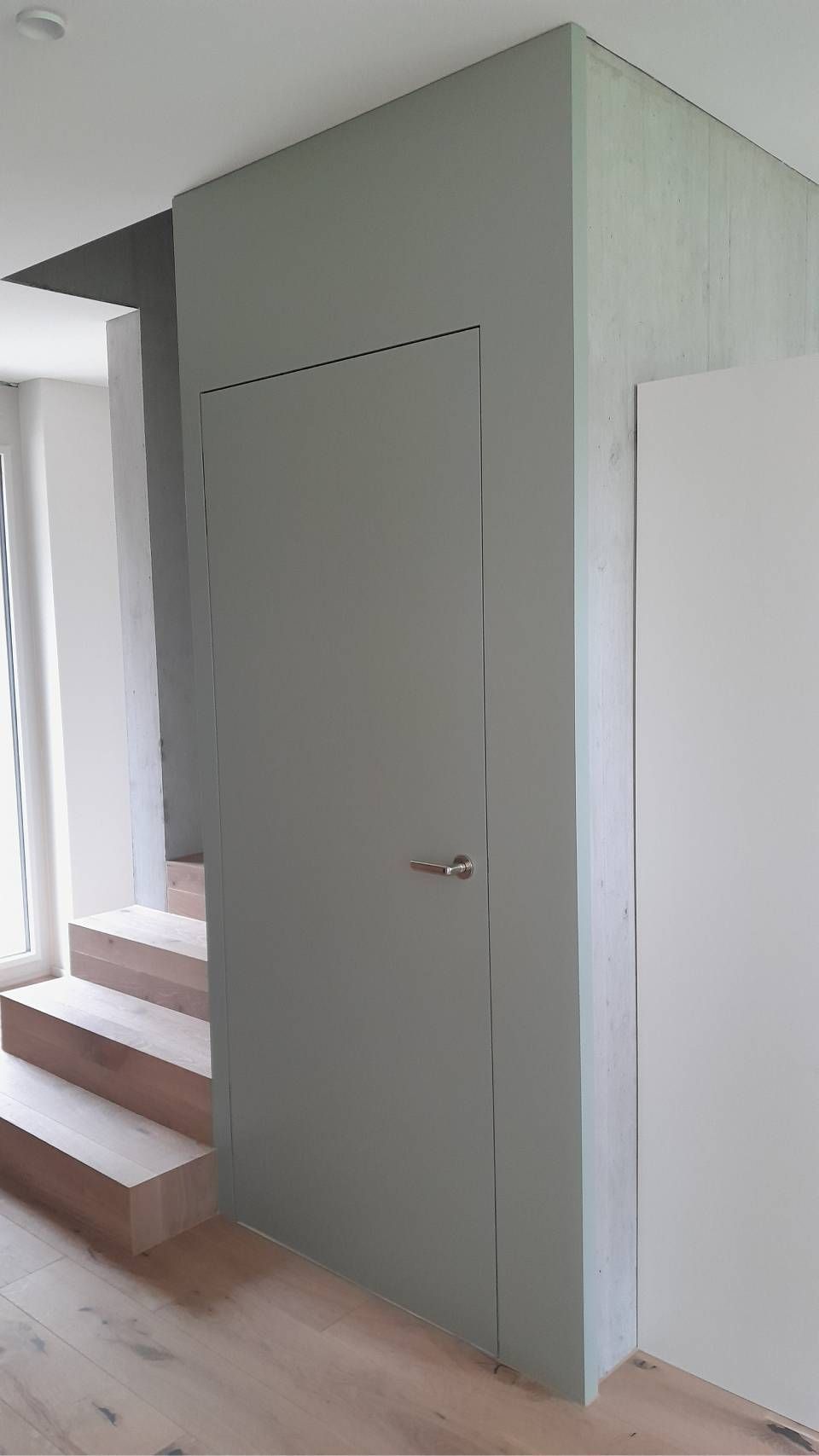 Kleine, hellgrüne Einbautür neben einer Treppe in einem hellen Flur.