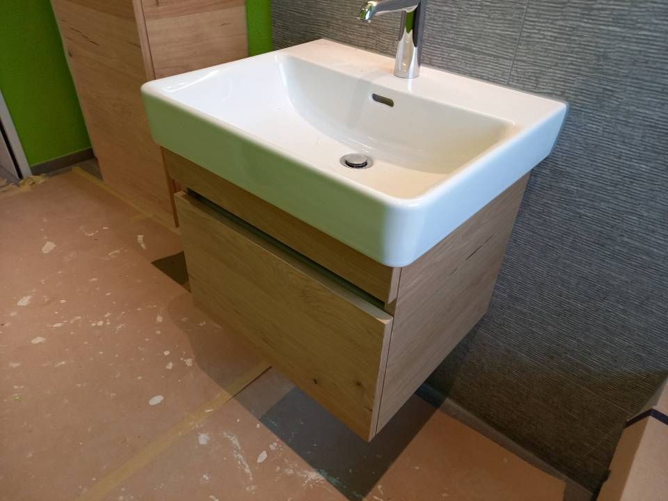 Badezimmerwaschtisch mit weissem Becken und hellem Holzschrank vor einer mit Teppich ausgelegten Wand.