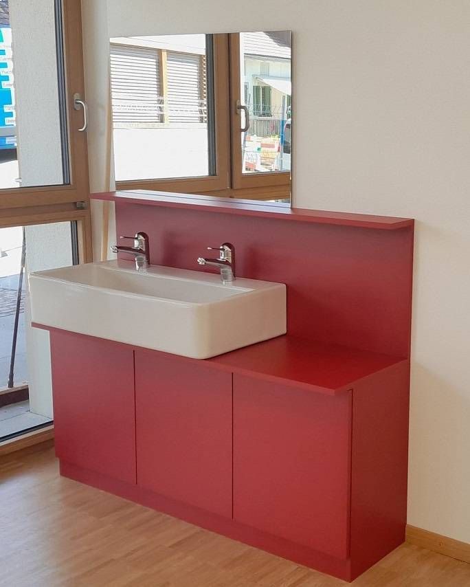 Roter Waschtisch mit weissem Waschbecken und Spiegel vor einer hellen Wand