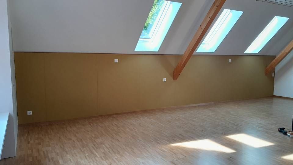 Leeres Dachzimmer mit schrägen Dachfenstern, Holzbalken und Sonnenlicht auf dem Boden
