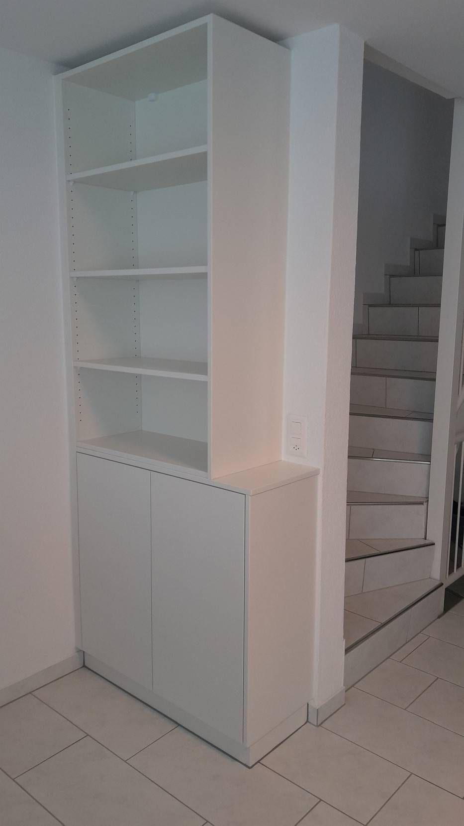 Weisse Einbauregale und ein Schrank neben einer Treppe in einem kleinen Zimmer.