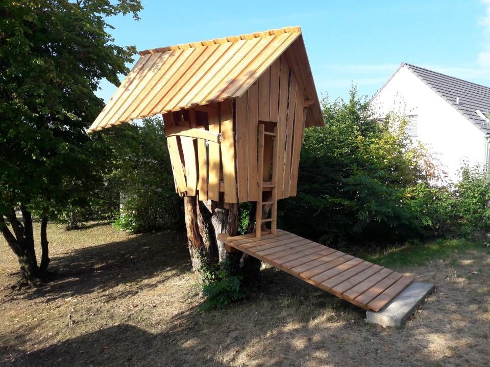 Kleines hölzernes Baumhaus auf Stelzen mit schrägem Dach und Rampe in einem grasbewachsenen Hof