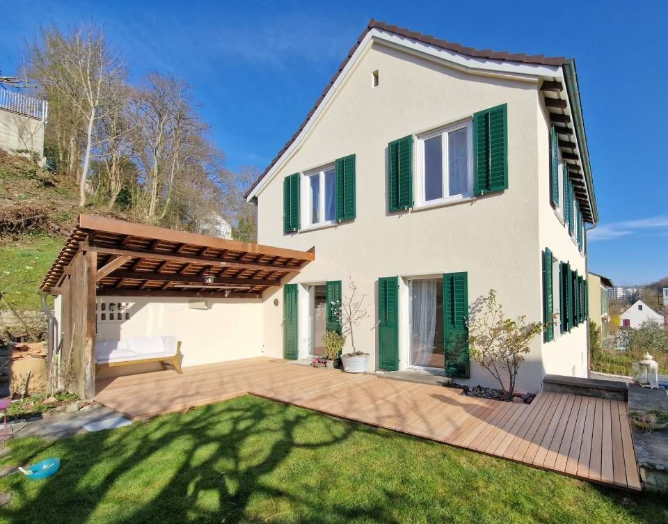 Cremefarbenes zweistöckiges Haus mit grünen Fensterläden, Terrasse, Pergola und Rasen im hellen Sonnenlicht