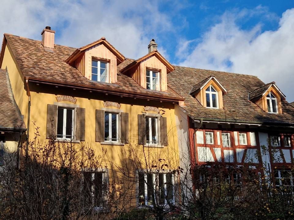 Eine sonnenbeschienene Reihe rustikaler Häuser mit Dachgauben und einem teilweise bewölkten blauen Himmel