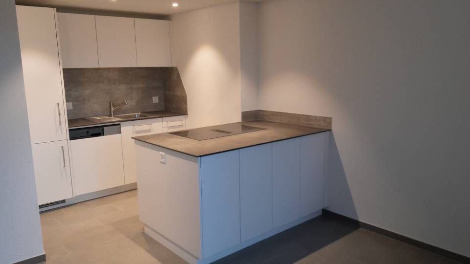Moderne Küche mit weissen Schränken, grauem Fliesenspiegel und einer zentralen Kochinsel unter sanfter Beleuchtung