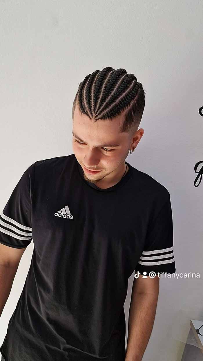 Un hombre con trenzas en el pelo lleva una camiseta adidas negra.