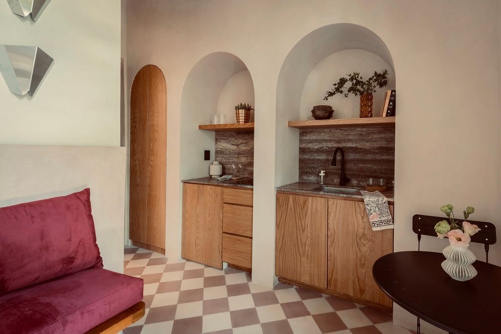 Interior with three alcoves: two with small wood kitchenettes, one with a wood door. A small table and sofa are visible.