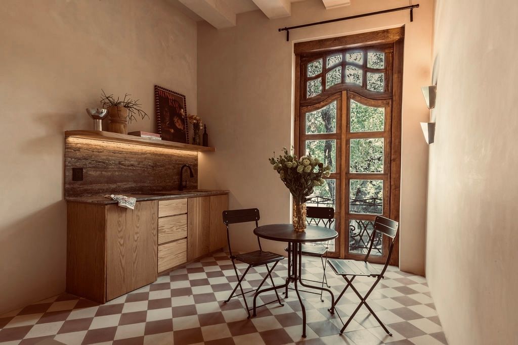 Small kitchen with wooden cabinets, checkered floor, round table and chairs, and a large arched window.