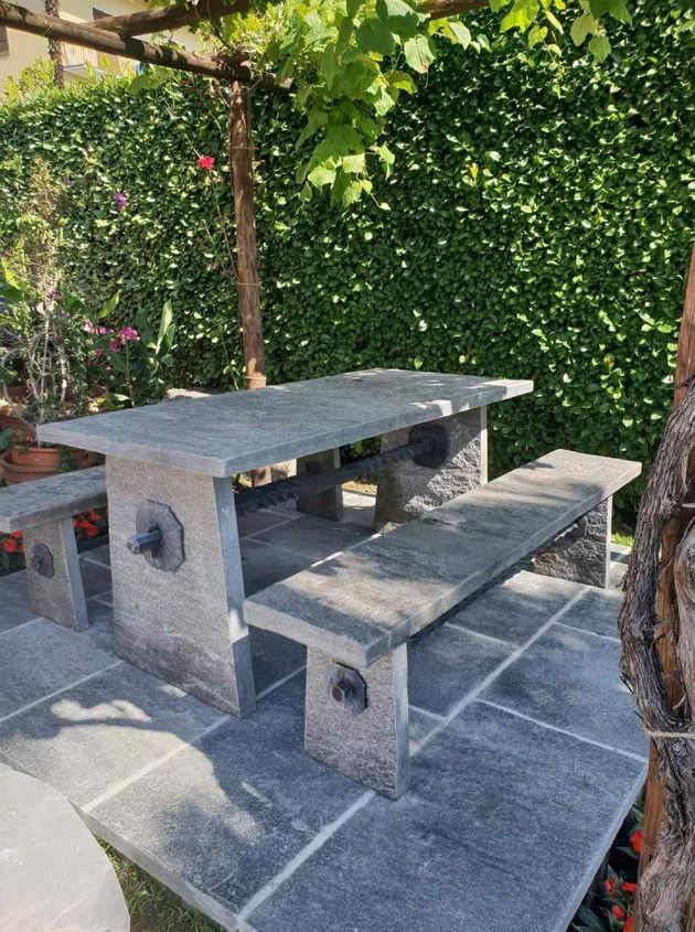 Tavolo e panchine in pietra su un patio accanto a una siepe verde e rigogliosa.