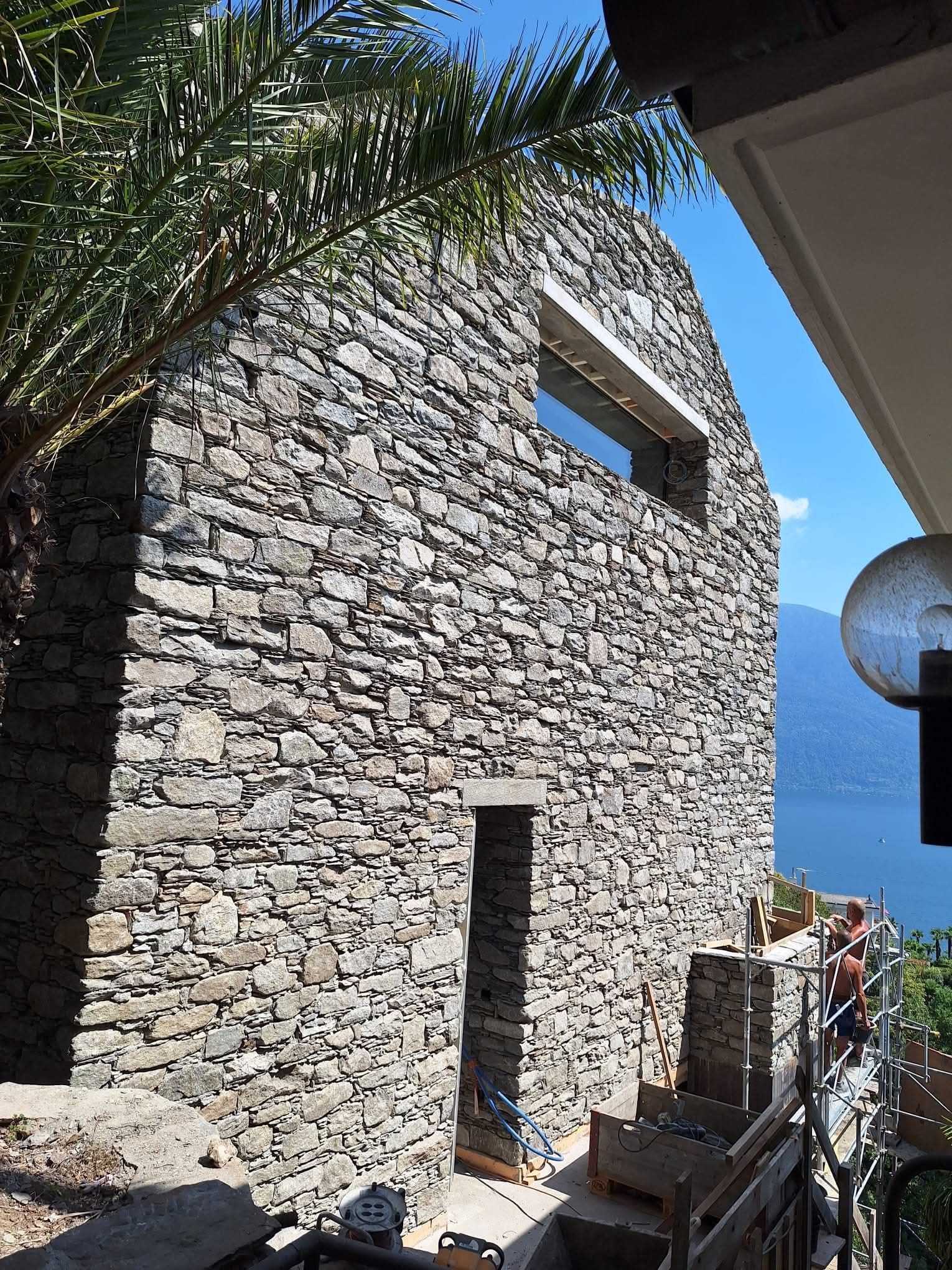 Terrasse eines modernen Hauses mit Glasgeländer, Steinmauer und Essbereich im Freien mit Panoramablick.