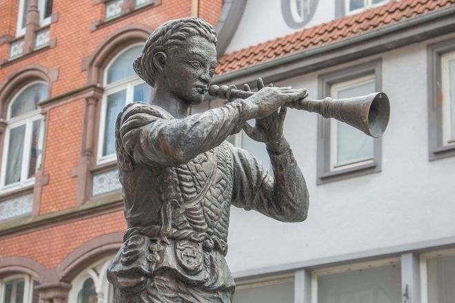 Eine Statue des Rattenfängers, der vor einem Backsteingebäude Trompete spielt.