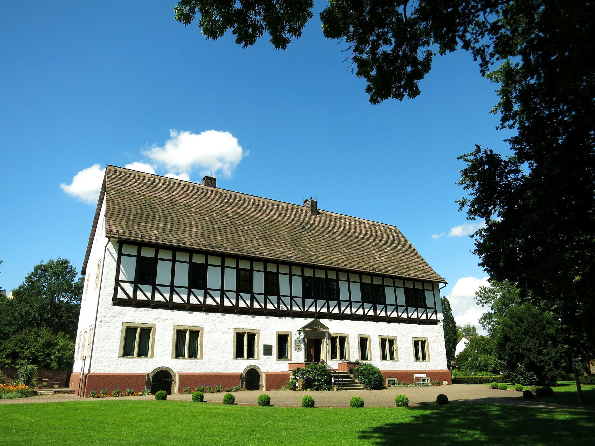 Ein großes weißes Haus mit einem braunen Dach liegt inmitten eines üppigen grünen Feldes