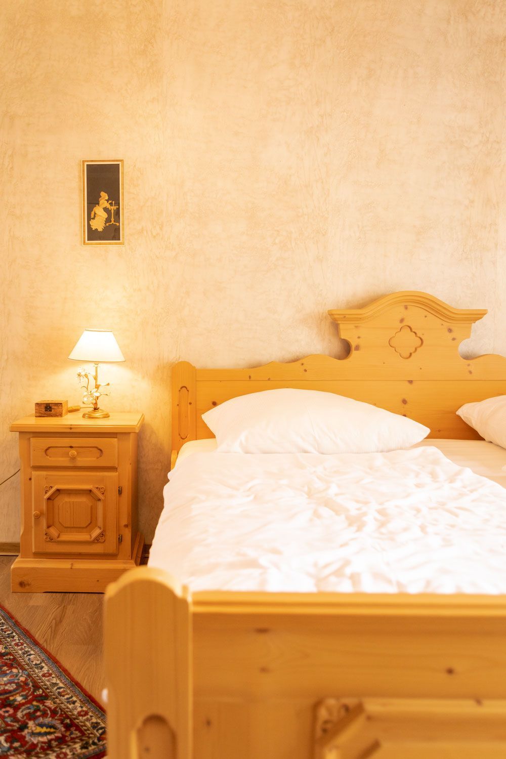 Ein Schlafzimmer mit Holzbett, Nachttisch, Lampe und Teppich.