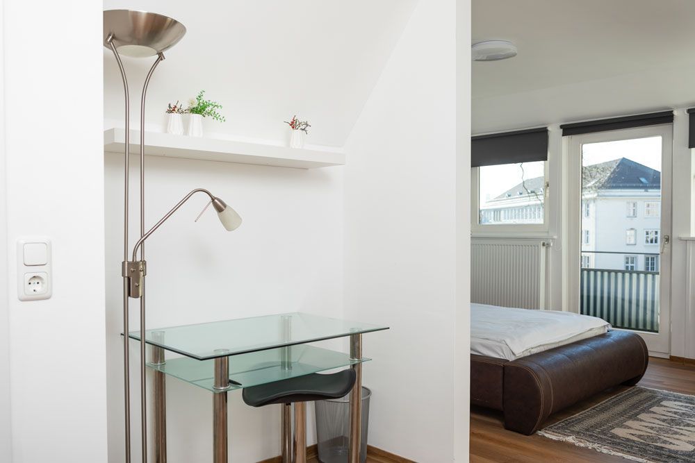 Ein Schlafzimmer mit einem Glasschreibtisch und einer Lampe neben einem Bett.