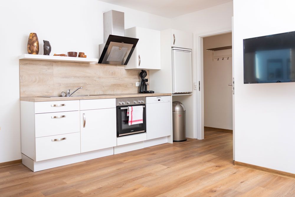 Eine moderne Küche mit weißen Schränken, einer hellen Holzarbeitsplatte, Edelstahlgeräten und einem an der Wand montierten Fernseher.