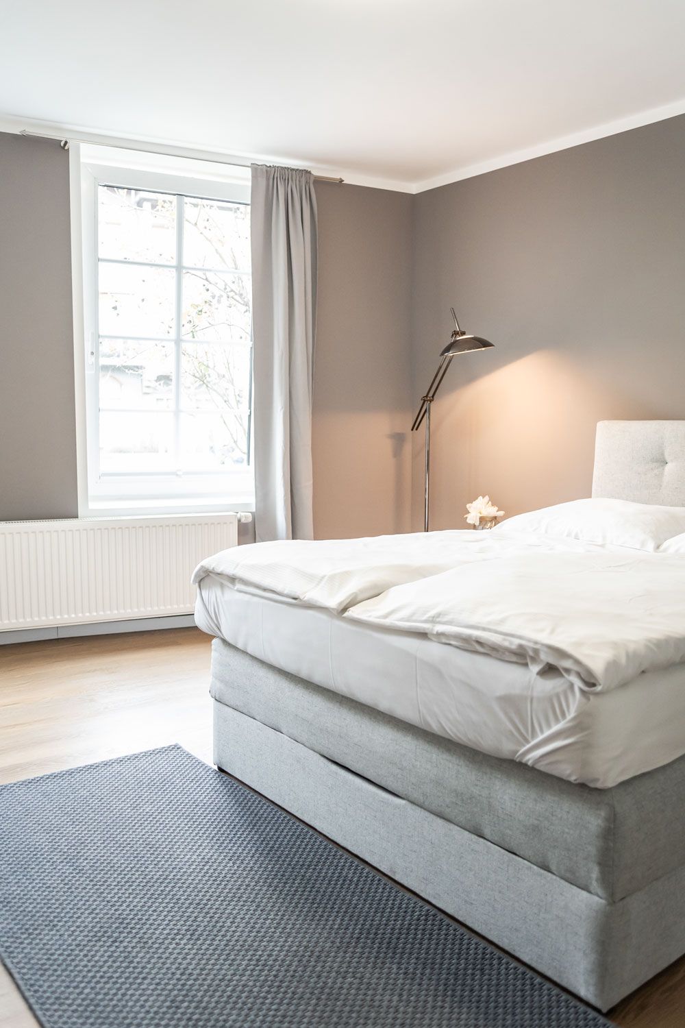 Ein Schlafzimmer mit Bett, Teppich, Lampe und Fenster.