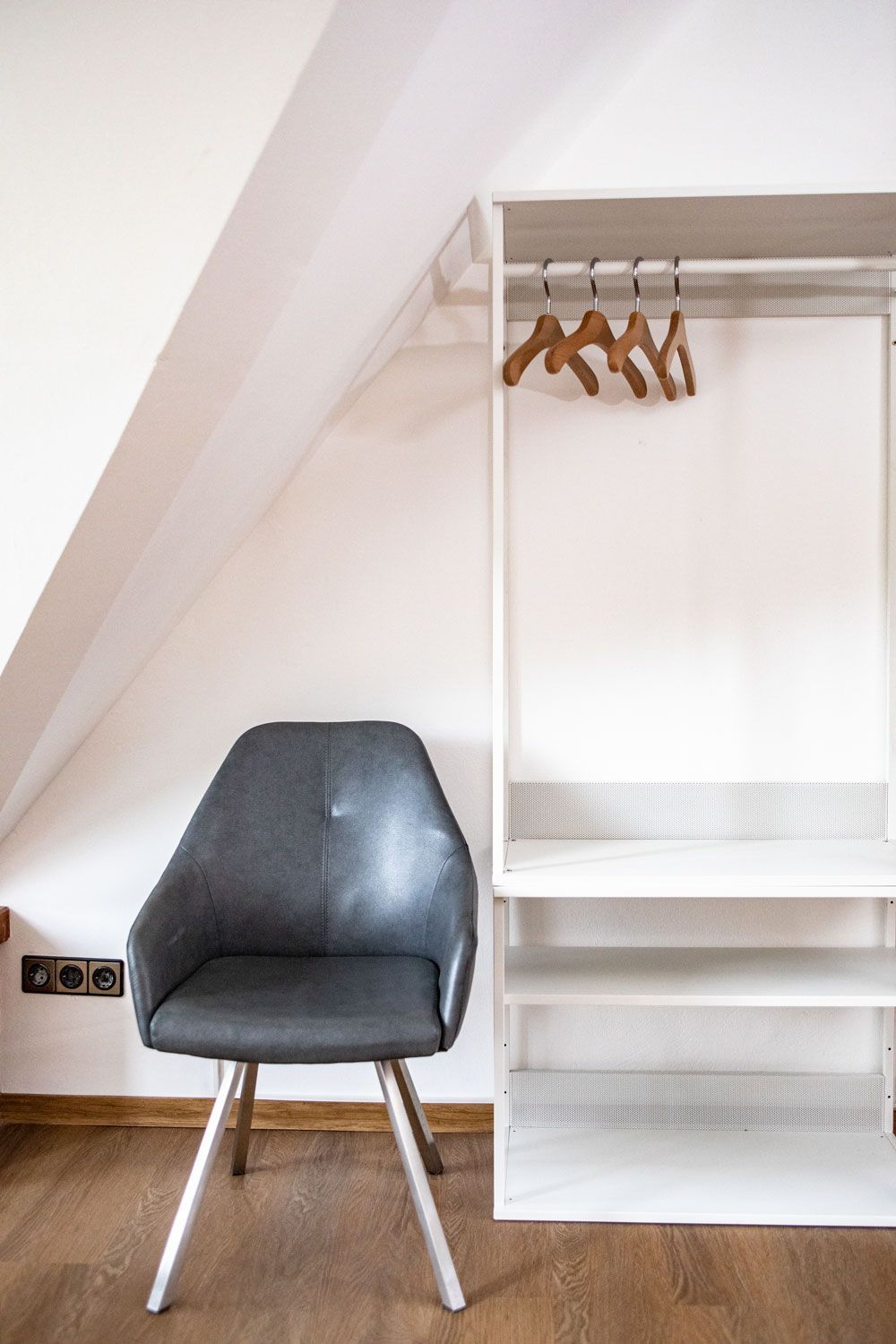 Neben einem Schrank steht ein Stuhl, an dem Kleidung hängt.